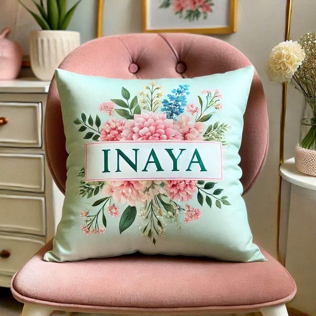 Un coussin personnalise avec le prenom inaya couleur rose pastel fleuri et vert deau pose sur une chaise elegant